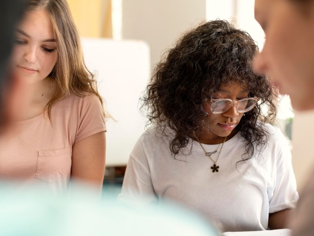 Trois femmes adultes concentrées et attentives durant un atelier d'échange et de partage chez Harmonie Apprentissage.
