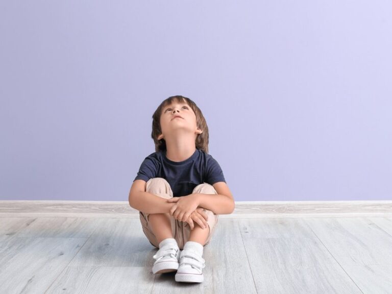 Petit garçon assis par terre regardant vers le haut, symbolisant la neurodiversité et une perception différente du monde chez l'enfant autiste.