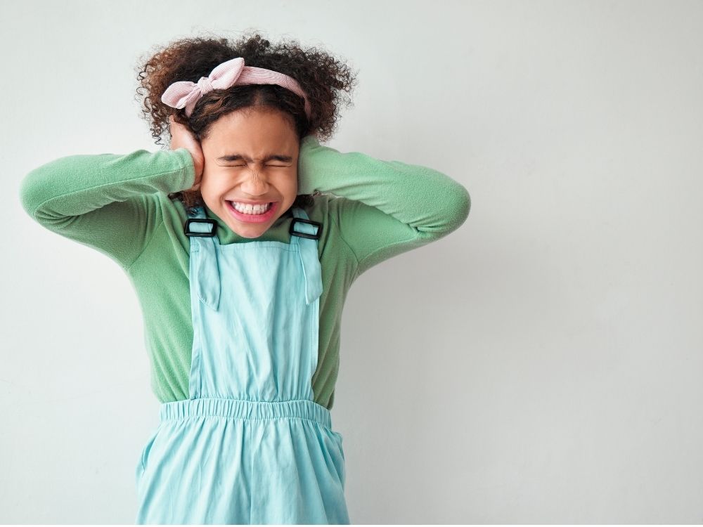 Jeune fille autiste se bouchant les oreilles, illustrant l'hypersensibilité sensorielle et la surcharge face au bruit.