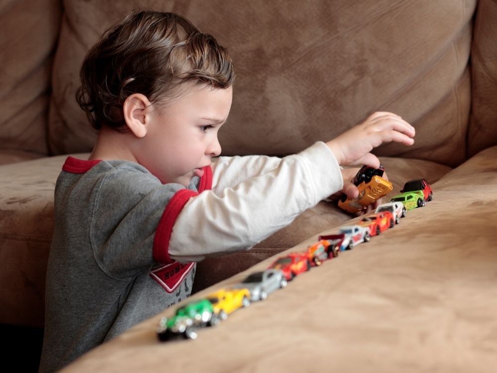 Un jeune enfant autiste, vu de profil, aligne minutieusement des voitures de couleurs, illustrant un jeu stéréotypé.