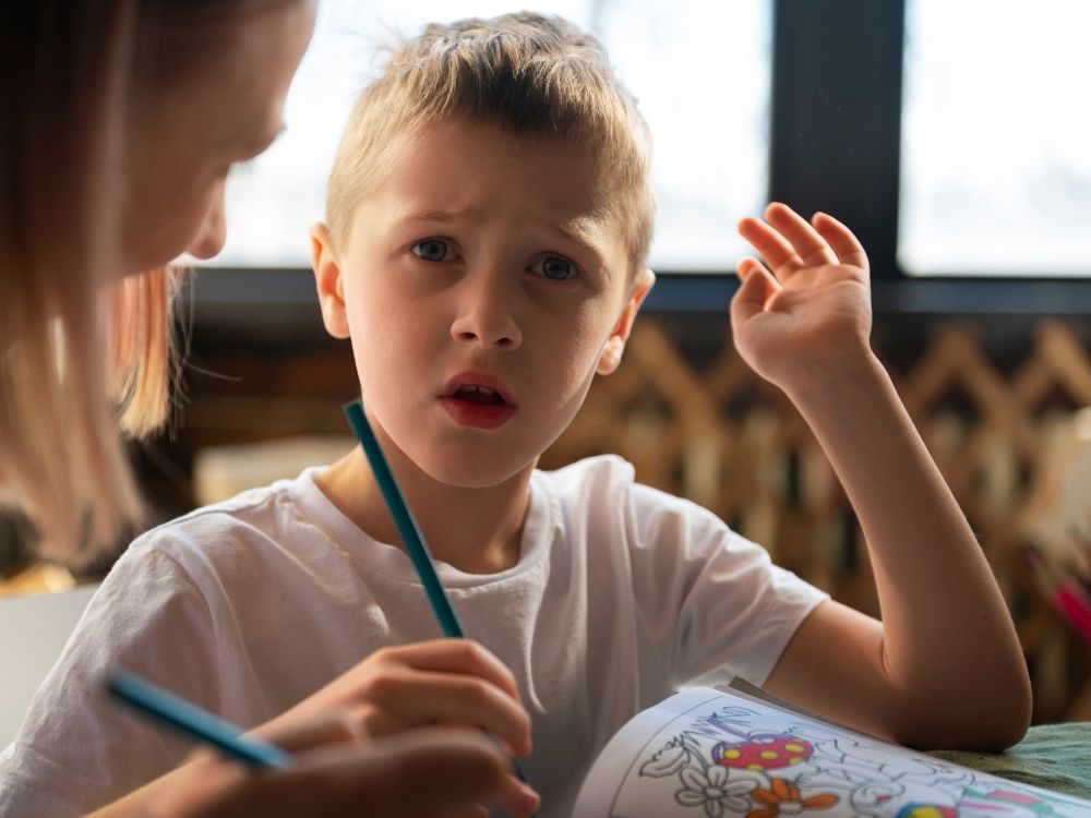 Enfant autiste en classe bénéficiant d'aménagements scolaires et du soutien d'une AESH pour réaliser ses exercices.