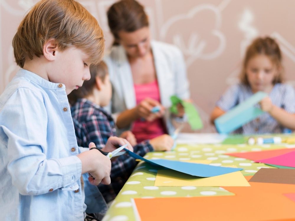 Élèves en classe ULIS réalisant des activités manuelles avec l'aide d'une enseignante, illustrant le cadre scolaire spécialisé pour l'autisme.