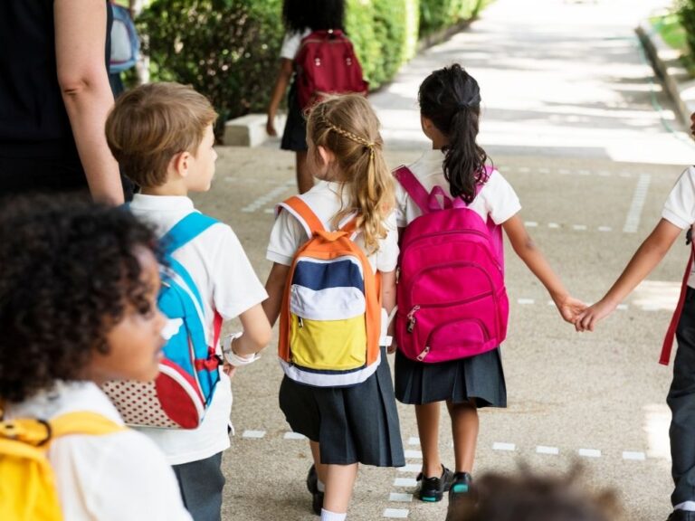 Groupe d'enfants avec des sacs à dos marchant ensemble vers l'école, illustrant l'inclusion scolaire pour les enfants autistes.
