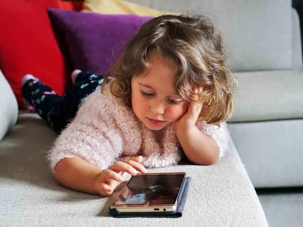 Petite fille captivée par un téléphone portable posé sur un canapé.