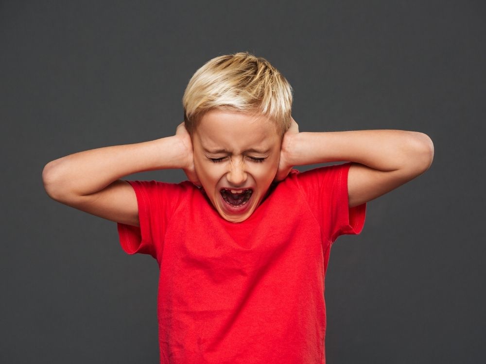 Garçon se bouchant les oreilles et criant face à une surcharge sensorielle.