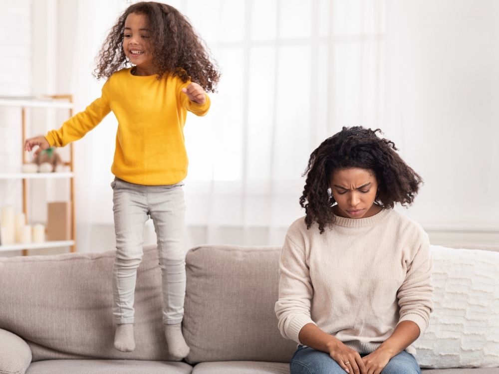 Enfant débordante d'énergie sautant sur le canapé à côté de sa mère fatiguée.