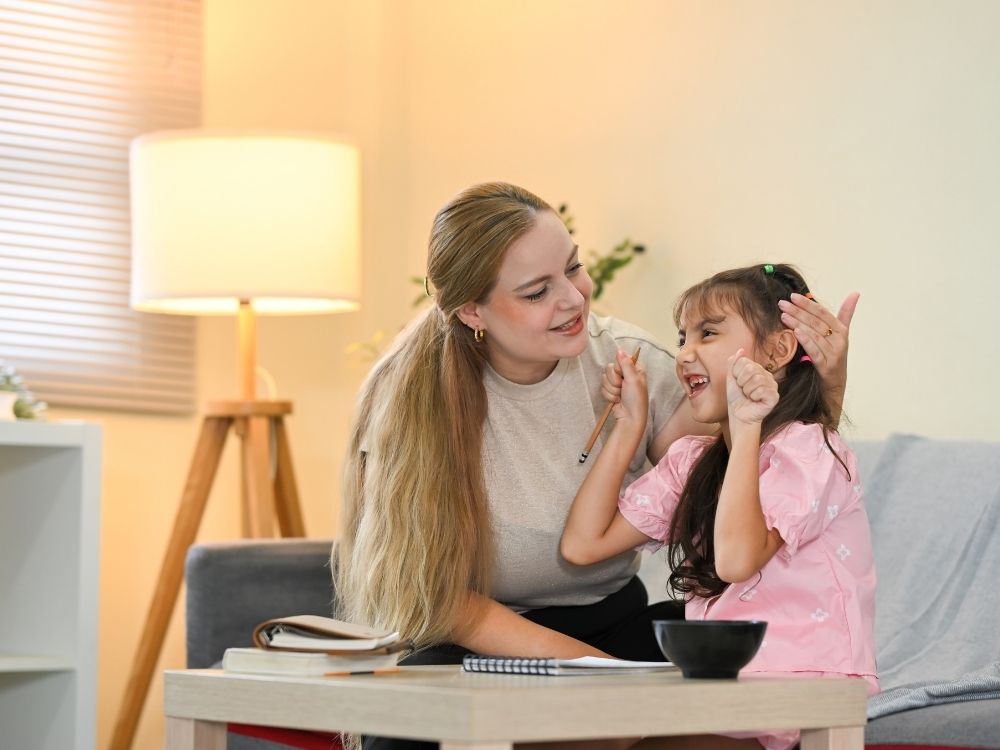 Enfant souriante et parent complice célébrant la réussite d'un devoir duite à l'application des conseils concrets appris en coaching parental à Thionville