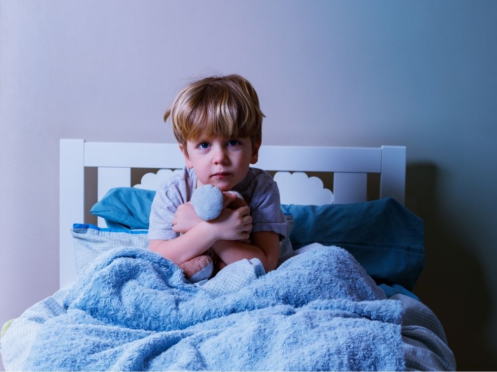 Garçon insomniaque assis dans son lit, illustrant les troubles du sommeil de l'enfant et les nuits agitées.