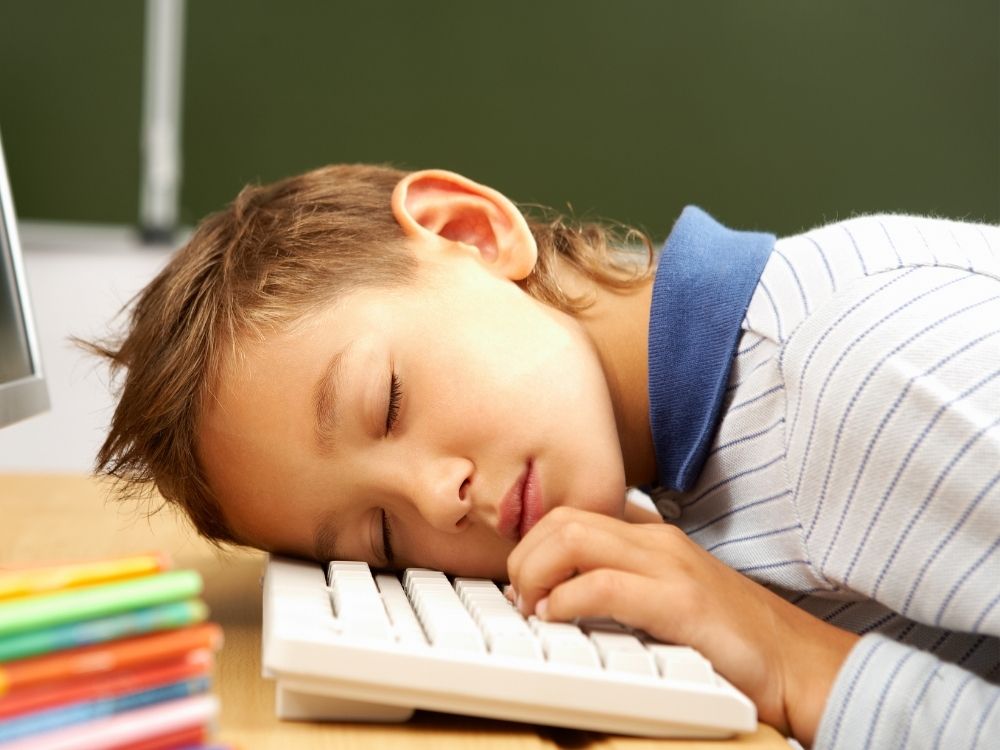 Jeune garçon endormi sur son bureau illustrant la fatigue diurne intense et l'épuisement scolaire causés par des troubles du sommeil profonds.