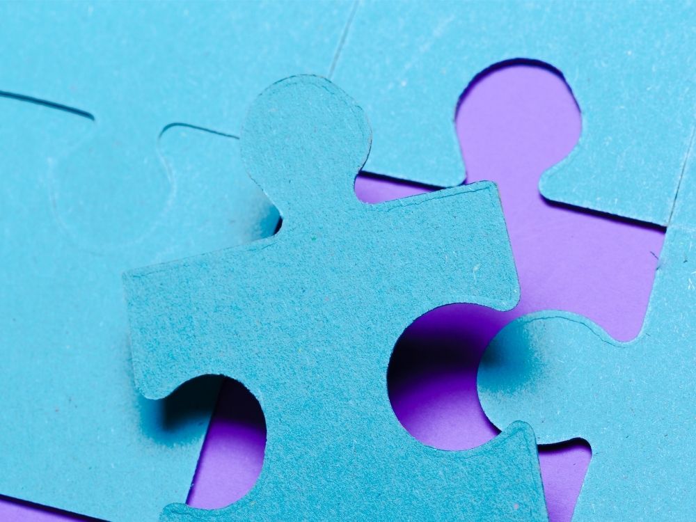 Pièces de puzzle bleues mal alignées sur un fond violet, illustrant les difficultés de connexion liées à l'autisme.