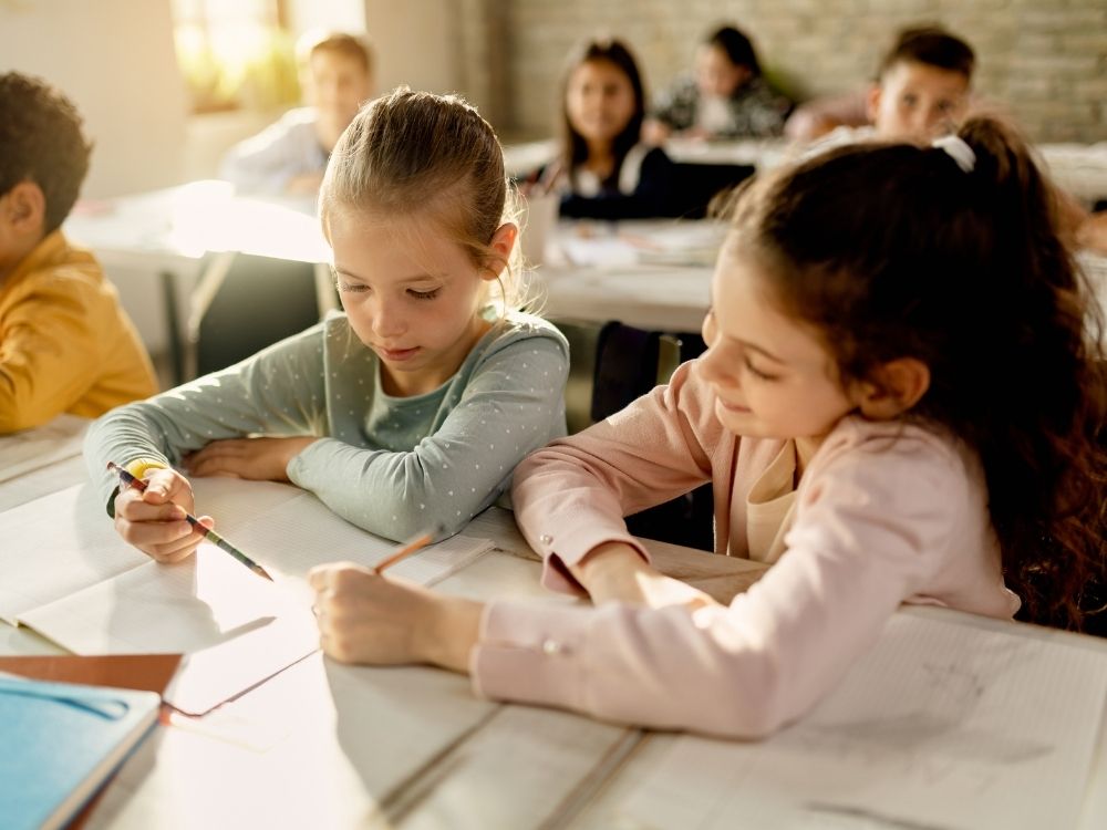 Deux enfants concentrés sur leur cahier en classe lors d'une intervention à l'école par Harmonie Apprentissage.