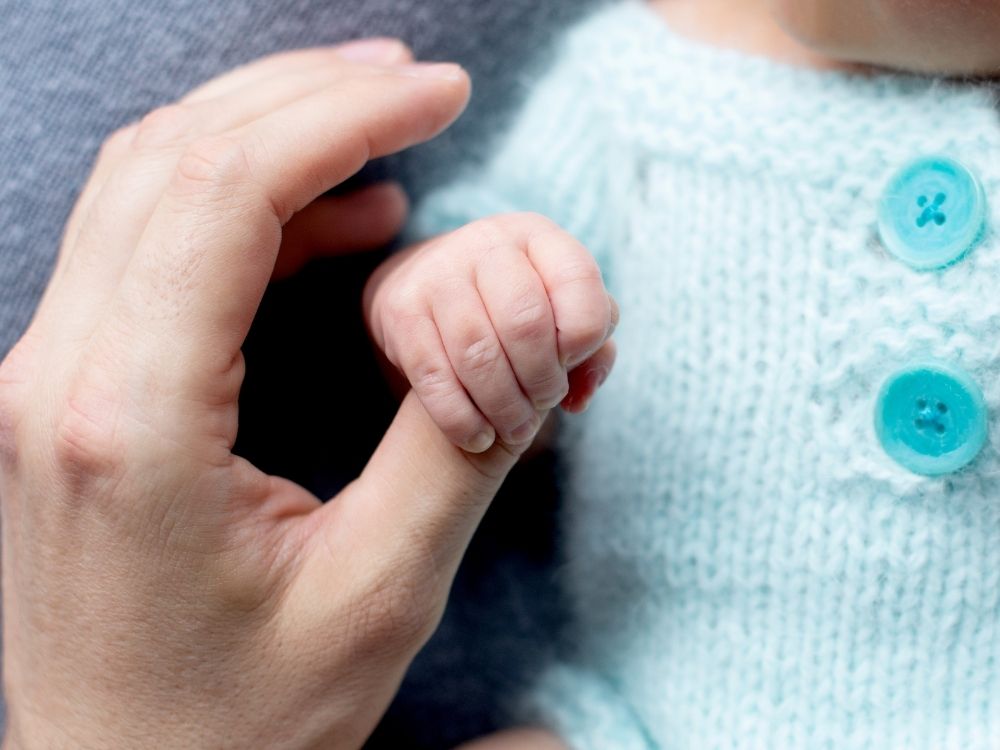 Main d'un nouveau-né qui agrippe le doigt d'un adulte, illustrant le réflexe archaïque d'agrippement et l'accompagnement d'Harmonie Apprentissage.