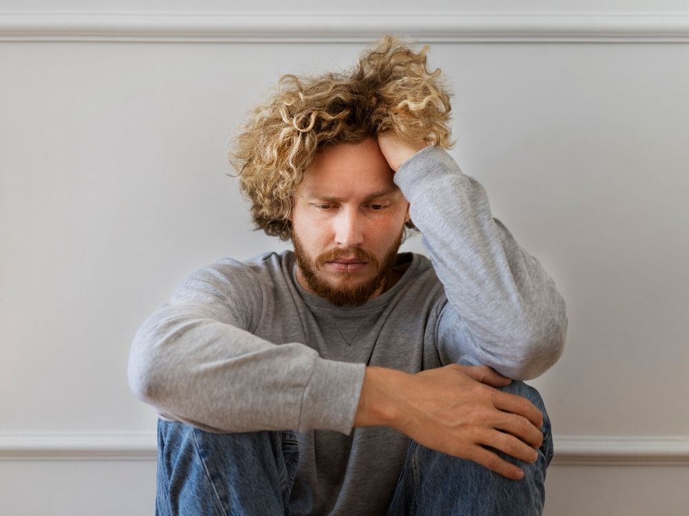 Homme penché la tête dans la main illustrant le suivi personnalisé pour adultes neurotypiques et neuroatypiques