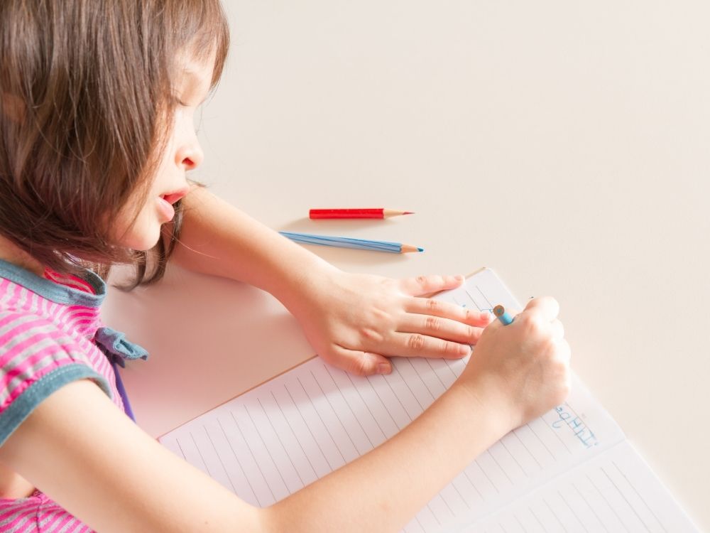 Petite fille avec des troube le l'apprentissage, concentrée qui s'applique à écrire sur un cahier d'école, illustrant le développement des compétences scolaires avec un touble d'apprentissage.