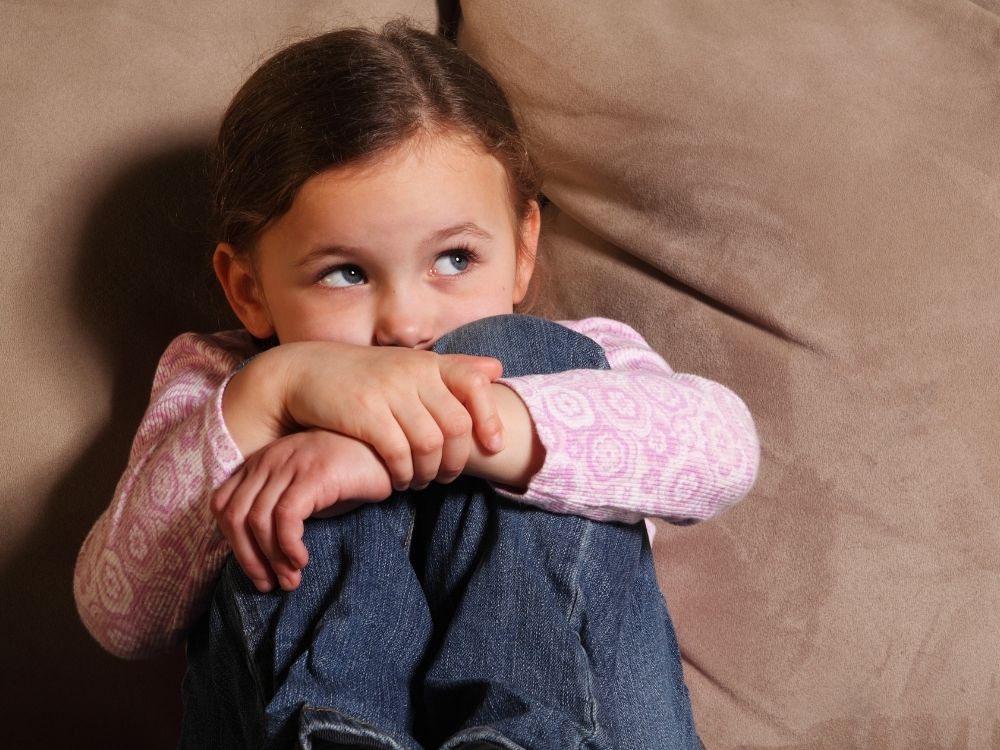 Petite fille recroquevillée sur un canapé, illustrant la sensibilité émotionnelle et l'accompagnement des troubles du neurodéveloppement.