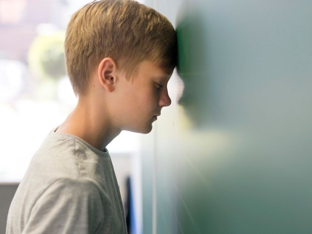 Jeune garçon appuyant son front contre un tableau vert dans une classe