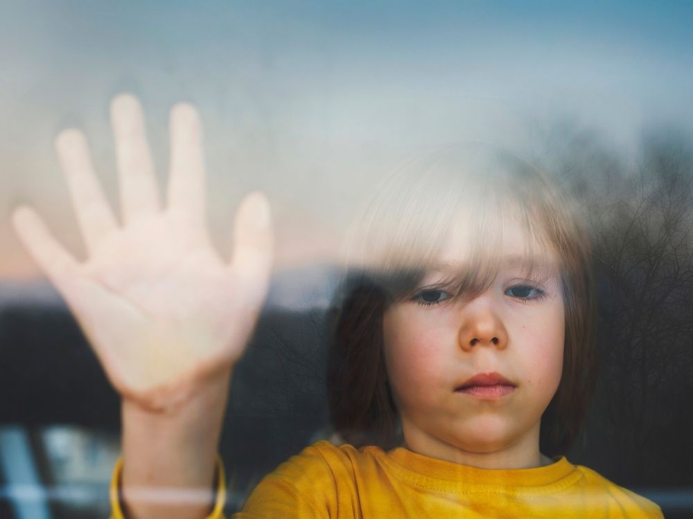Jeune enfant posant sa main contre une vitre avec un regard triste