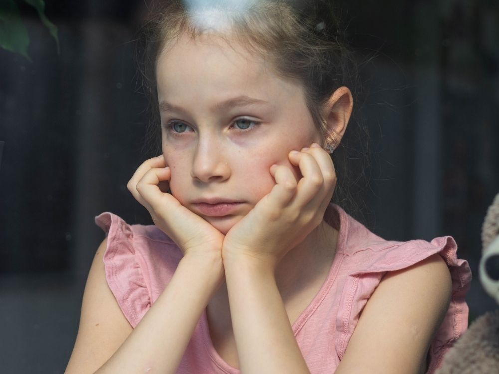 Fillette pensive et triste regardant à travers une fenêtre la tête appuyée sur ses mains