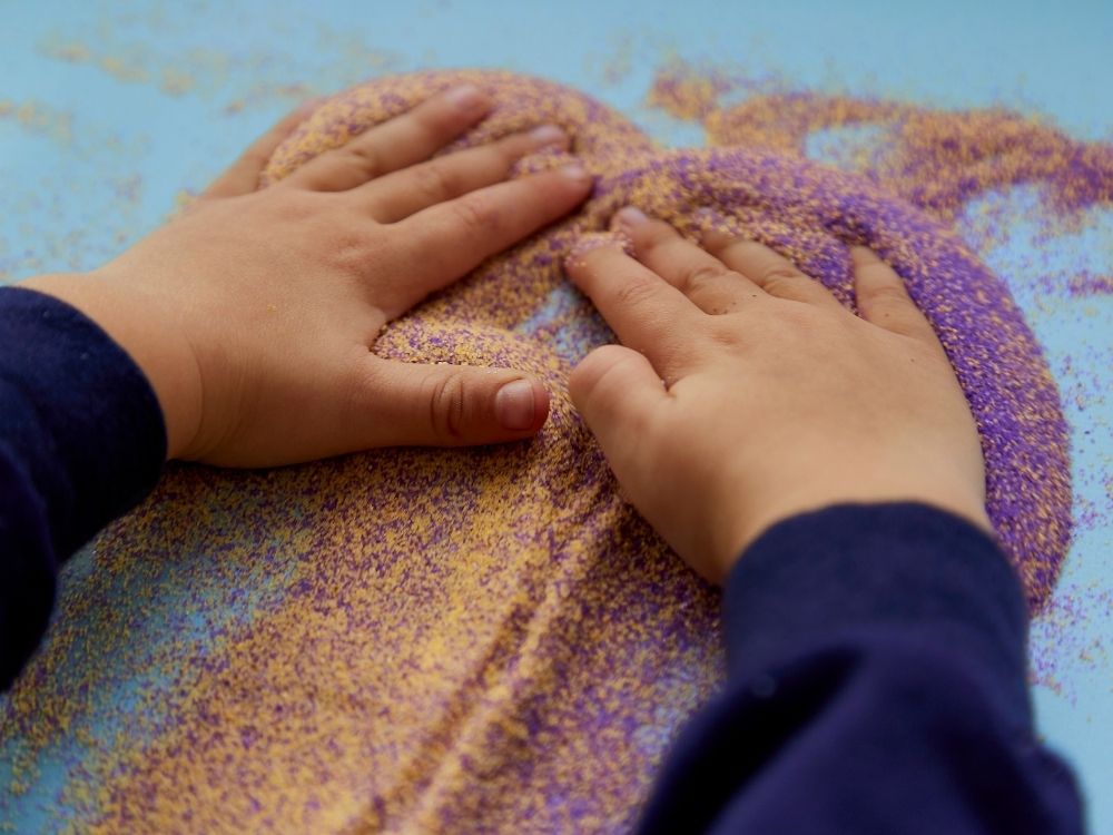 Mains d'enfant manipulant du sable coloré pour explorer les troubles sensoriels