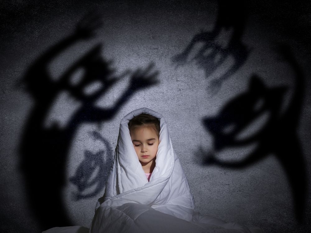 Enfant apeuré caché sous un drap entouré d'ombres terrifiantes de monstres