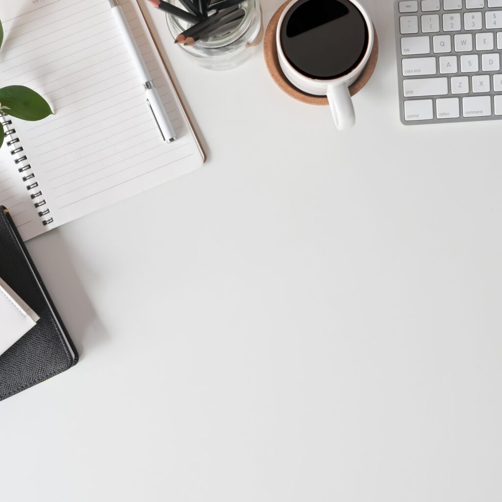 Vue d'en haut d'un bureau blanc épuré avec un carnet ouvert, un stylo, un clavier et une tasse de café
