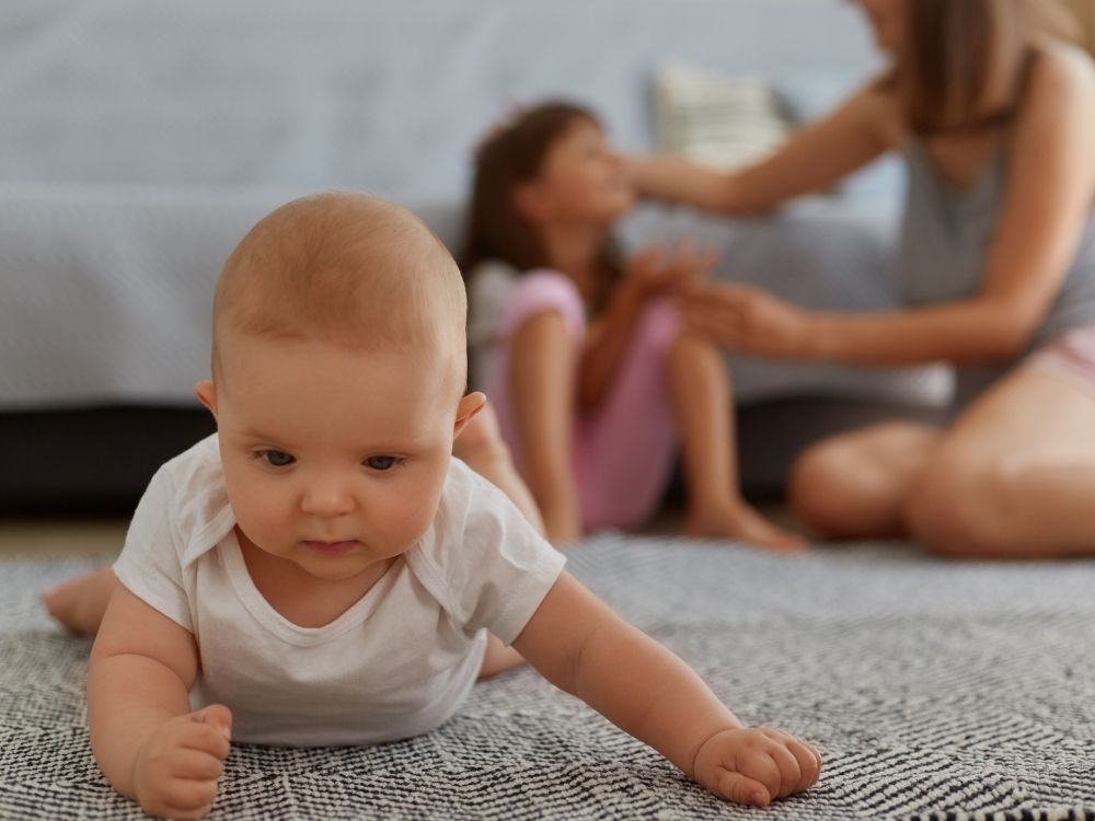 Bébé plat ventre sur un tapis travaillant son développement moteur sous le regard de sa mère